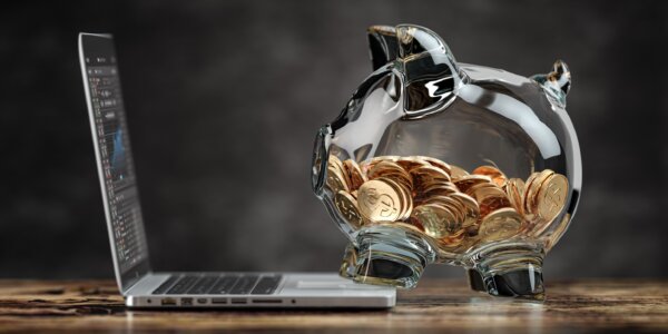 Image of a glass piggy bank of coins using a laptop showing financial info as illustration for post 'What can you claim if you're investing in your business?'