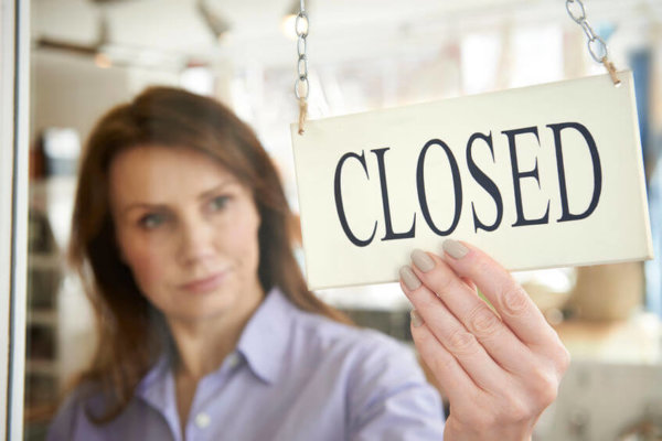 Image of female business owner with a 'closed' sign on the door as illustration for Blog Post 'Business Distress - what IS the true picture?'