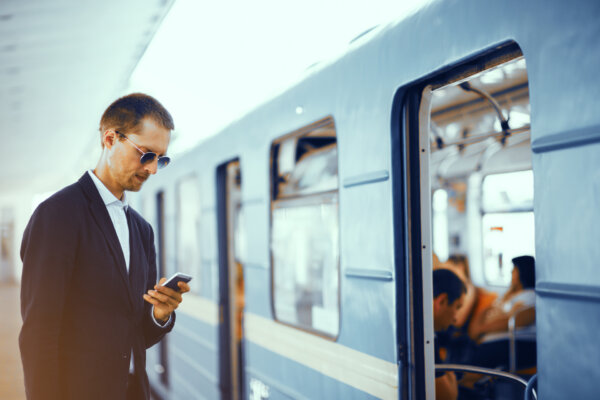 An image of a business traveller using their phone on a train station platform as illustration for post 'Hybrid working – what is 'a business journey'?'