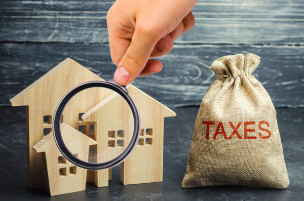 Image of wooden house under a magnifying glass as illustration for Post 'How is Property Taxed?'