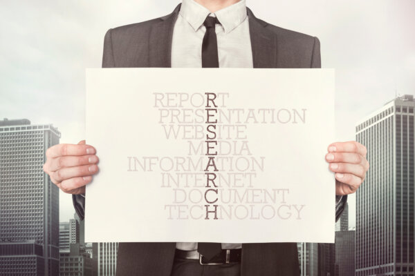 An image of a business owner holding up a notice with different aspects of research activity written to create the word 'research' through the middle, as illustration for post 'Research and Development Tax Credits: Myths and Facts.'