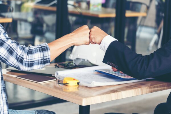 An image of two shareholders fist-bumping agreement across the desk, as illustration for post 'The importance of a shareholders agreement '