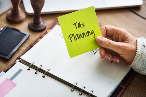 Image of business owner with planner open on the desk with various equipment around the desk and a sticky note with 'tax planning' written across it, as illustration for post 'End of Year Tax Planning Guide 2023/24'.