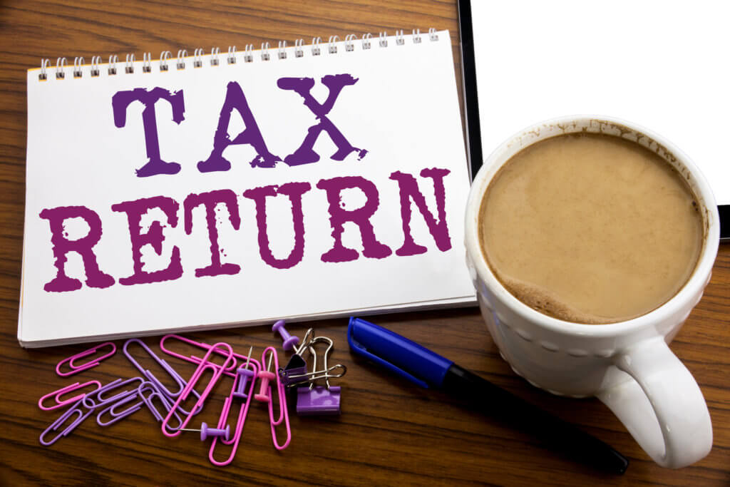 An image of a desk with 'Tax Return' written in large letters on a pad, with assorted stationery and a mug of tea as illustration for post 'What information do we need for your Personal Tax Return?'