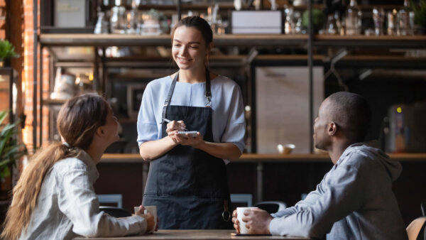 Image of a smiling waitress taking an order in a coffee shop as illustration for post 'New rules for distributing tips'