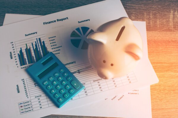 Image of a calculator and piggy bank sitting on top of coloured graphs as illustration for post 'Personal Financial Planning'.