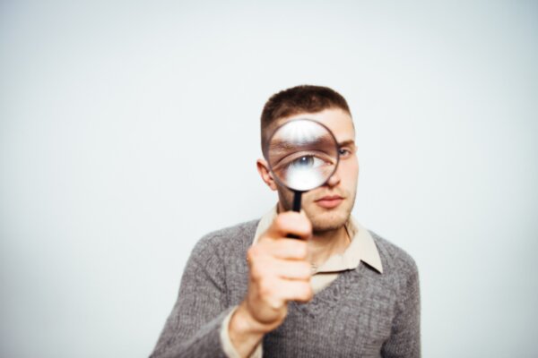 Image of a man in a grey jumper looking through a magnifying glass as illustration for post 'Red flags that can trigger unwanted interest from HMRC'.