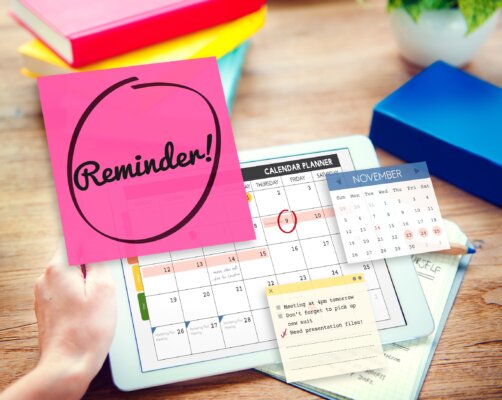 Image of a pink sticky note with the word 'reminder' written in black marker, alongside a calendar and other business stationery as illustration for post 'Minimum wage rates increase looming!'.